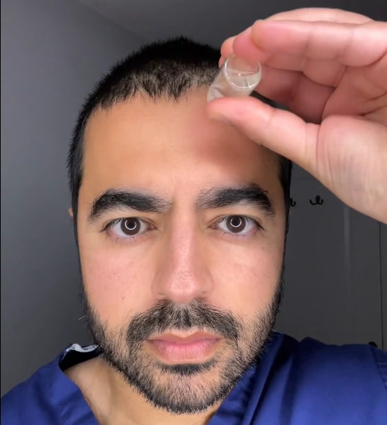 Person applying liquid to their scalp from a small vial.
